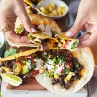 A hand pulling apart a ground beef taco showing the stretch of the cheese and toppings