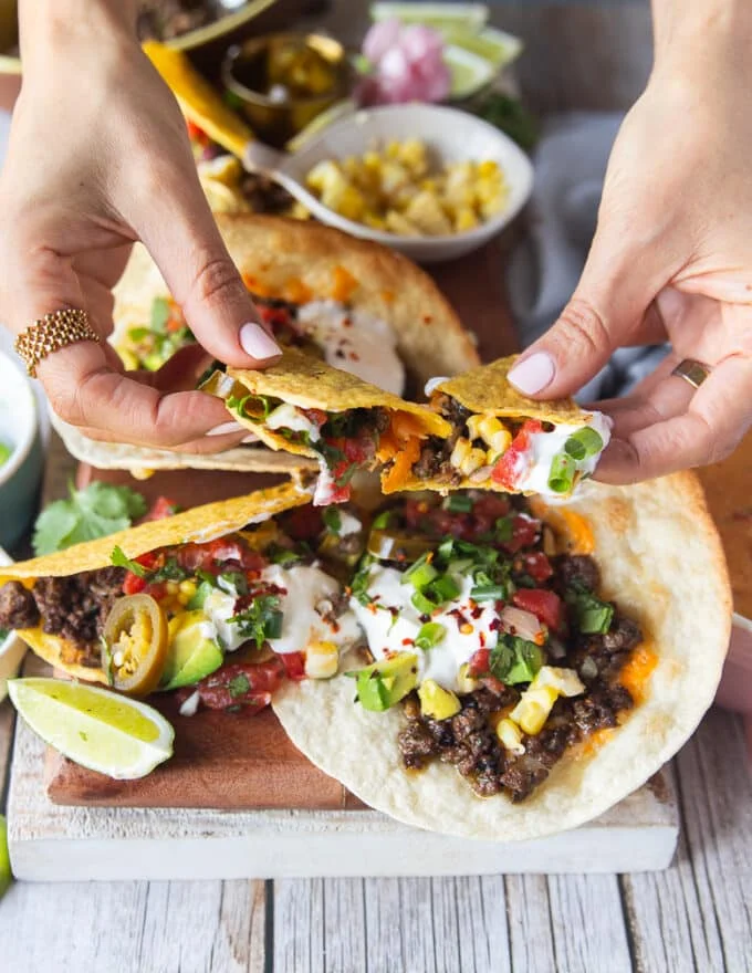 A hand pulling apart a ground beef taco showing the stretch of the cheese and toppings