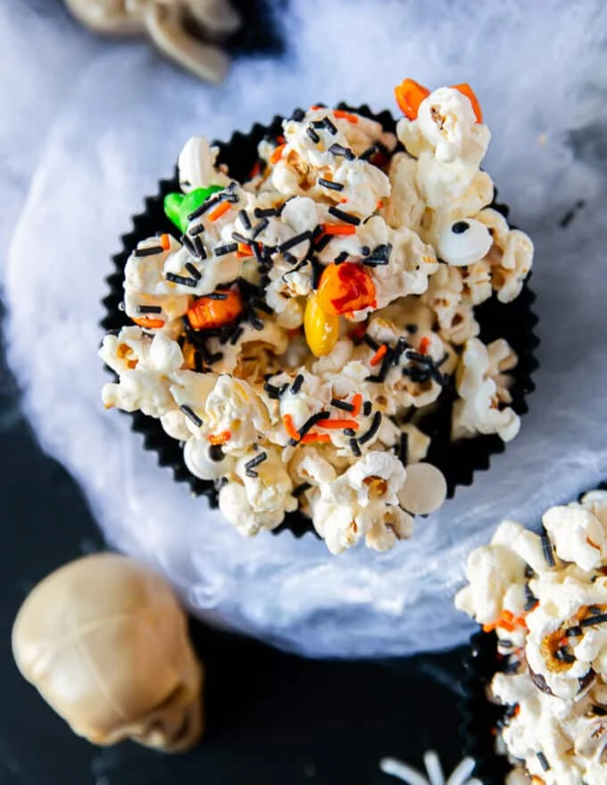 close up of a bowl of halloween popcorn sowing the black sprinkles, eye ball candies and orange candies stuck over the popcorn