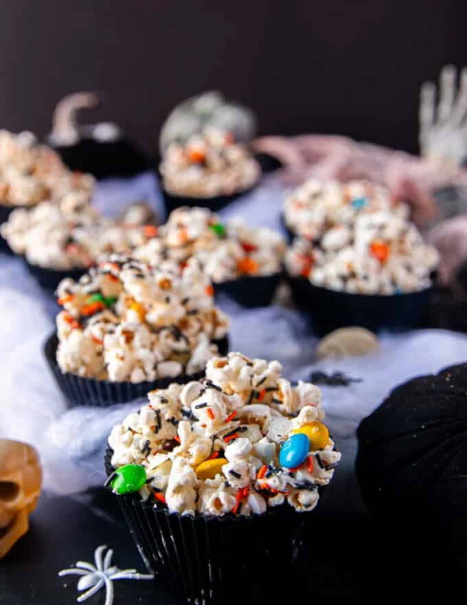 side view of halloween popcorn bowls arranged over white cloth like spider web surrounded by plastic mini skulls for a spooky setup