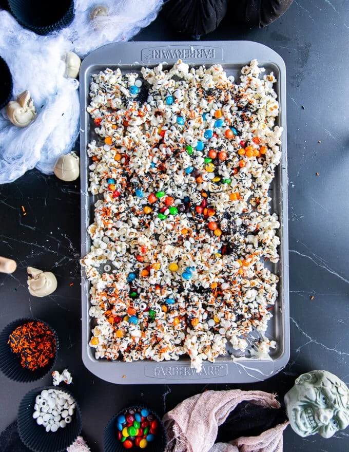 The tray of halloween popcorn sprinkled with spooky candies, black sprinkles, eyeball candies and more, ready to set