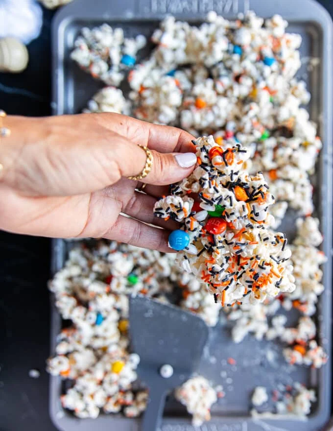 A hand holding a chunk of the halloween popcorn after it has set and all the spooky candy is showing