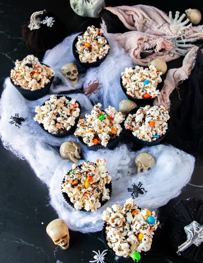 several cups of halloween popcorn on a black countertop surrounded by skulls