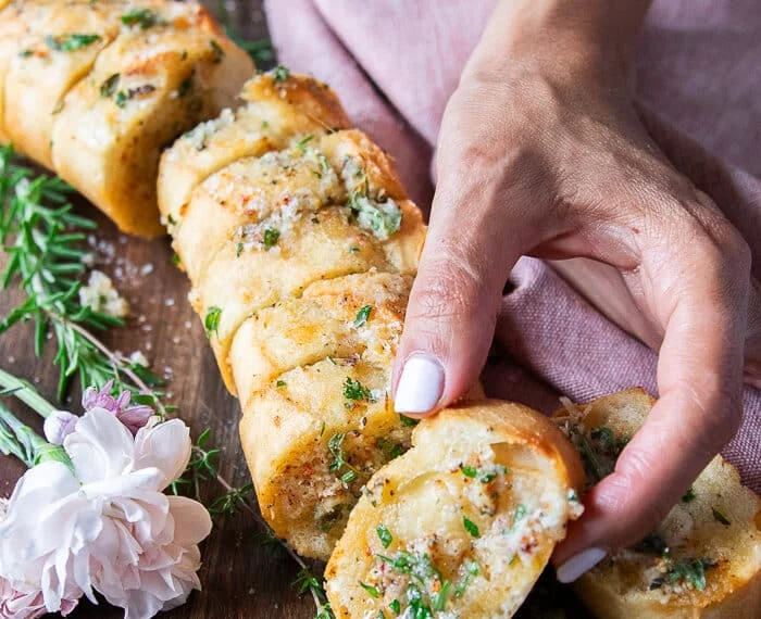 A hand holding one piece of air fryer garlic bread close up showing the texture and toppings