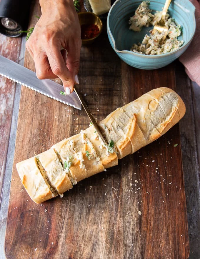 A hand using a spreading knife to spread the garlic butter in between the slices of bread and on the top as well covering it well and