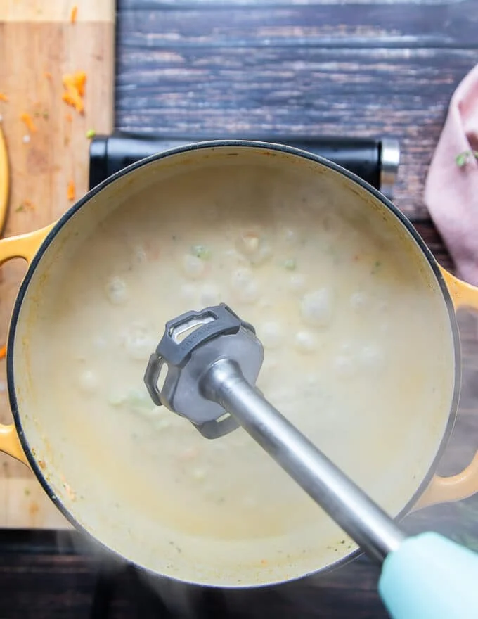 An immersion blender being used to puree the soup for those who like a smooth broccoli and cheddar soup recipe