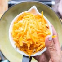 A hand holding in a bowl of shredded cheese ready to add them in to the soup