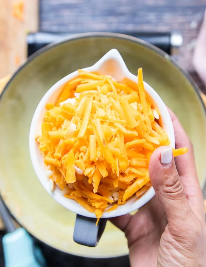 A hand holding in a bowl of shredded cheese ready to add them in to the soup