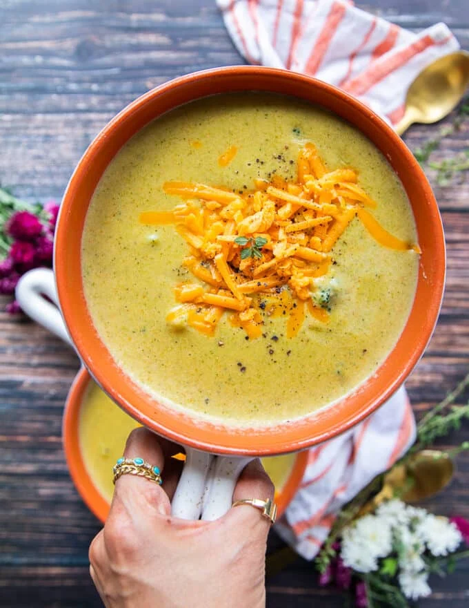 A hand holding a final bowl of cheddar broccoli soup close up showing the final texture and color