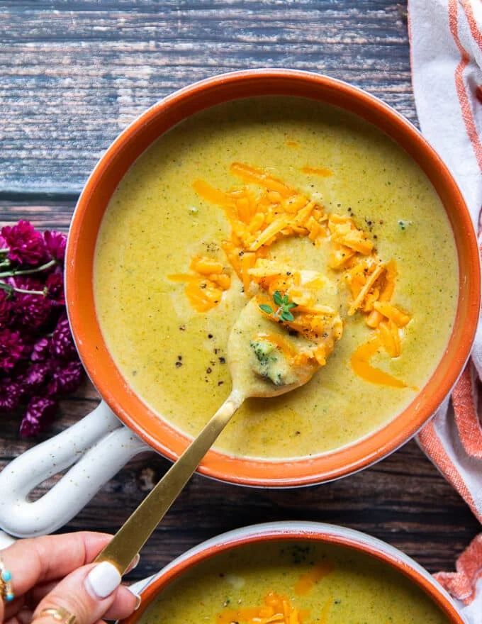 A hand spooning some broccoli cheddar soup in a bowl showing the chunks of broccoli and the silky creamy smooth soup