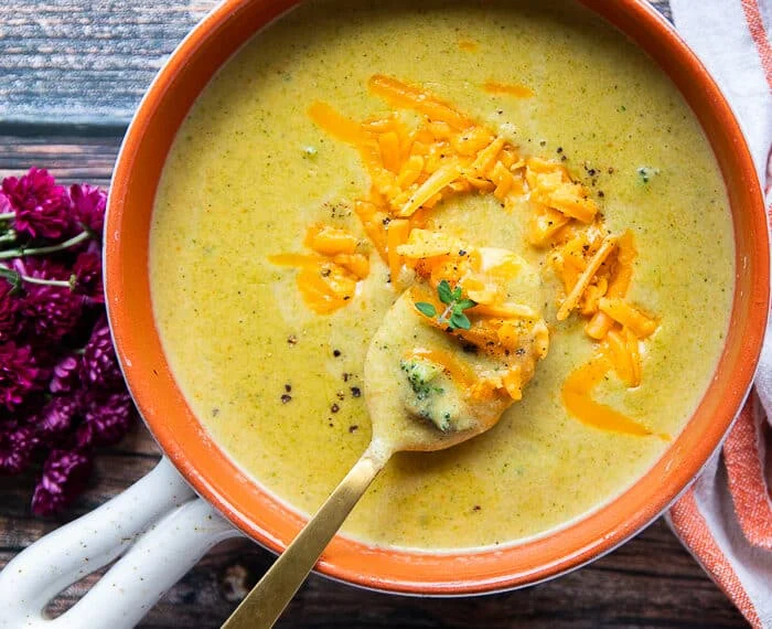 A hand spooning some broccoli cheddar soup in a bowl showing the chunks of broccoli and the silky creamy smooth soup