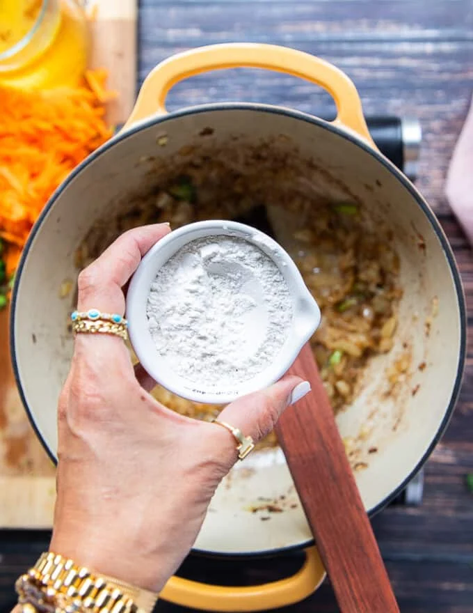 A hand holding the flour to add to the pot to make the roux in order to thicken the broccoli cheddar soup