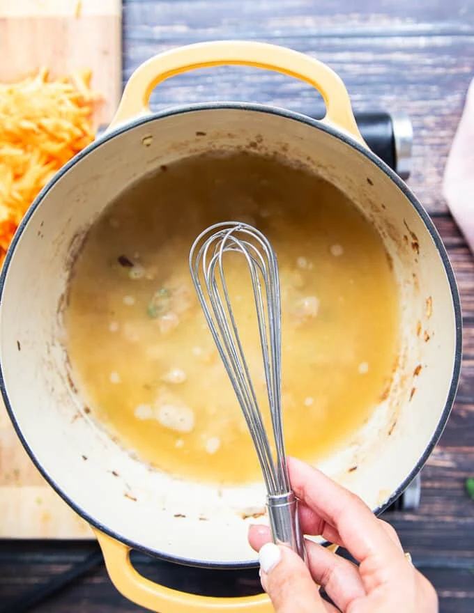 A hand holding a whisk to dissolve the roux into the stock