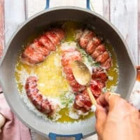 A spoon drenching the tops of the lobster tails with the butter sauce to help it cook the way through