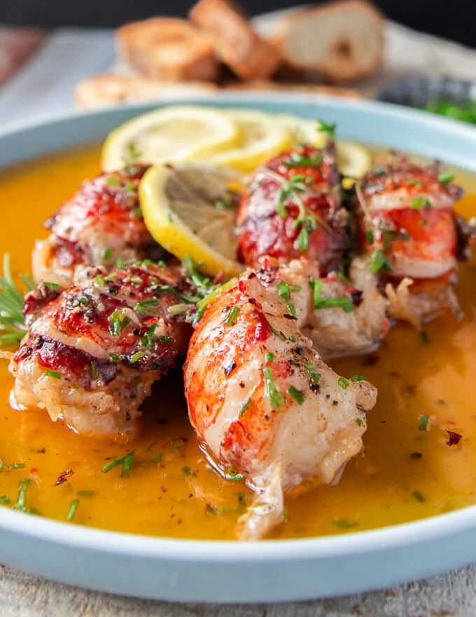 close up of a butter poached lobster showing the oink lobster and the golden flavored butter around it surrounded by lemon slices