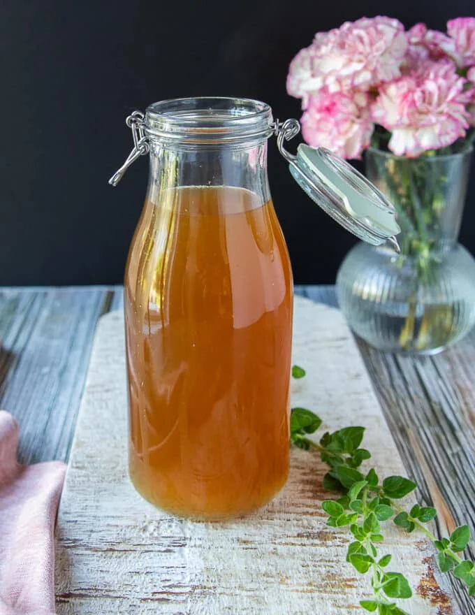 Lobster stock in a large jar showing the beautiful clear color of the stock and a some oregano around it