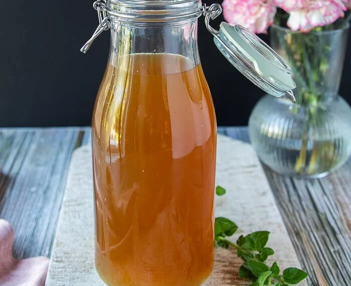 Lobster stock in a large jar showing the beautiful clear color of the stock and a some oregano around it