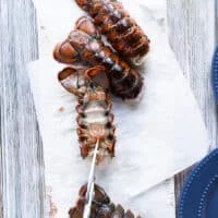 A hand holding a scissors and cutting through the back of the lobster to cut it open