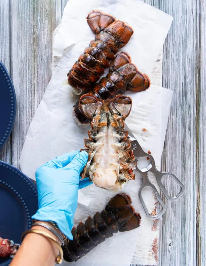 a hand wearing gloves and separating the lobster meat from the shell carefully