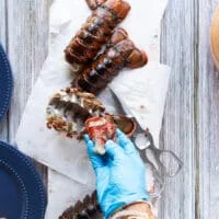 A hand wearing gloves pulling gently the lobster meat away from the shells