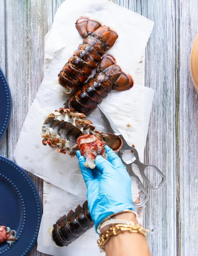 A hand wearing gloves pulling gently the lobster meat away from the shells