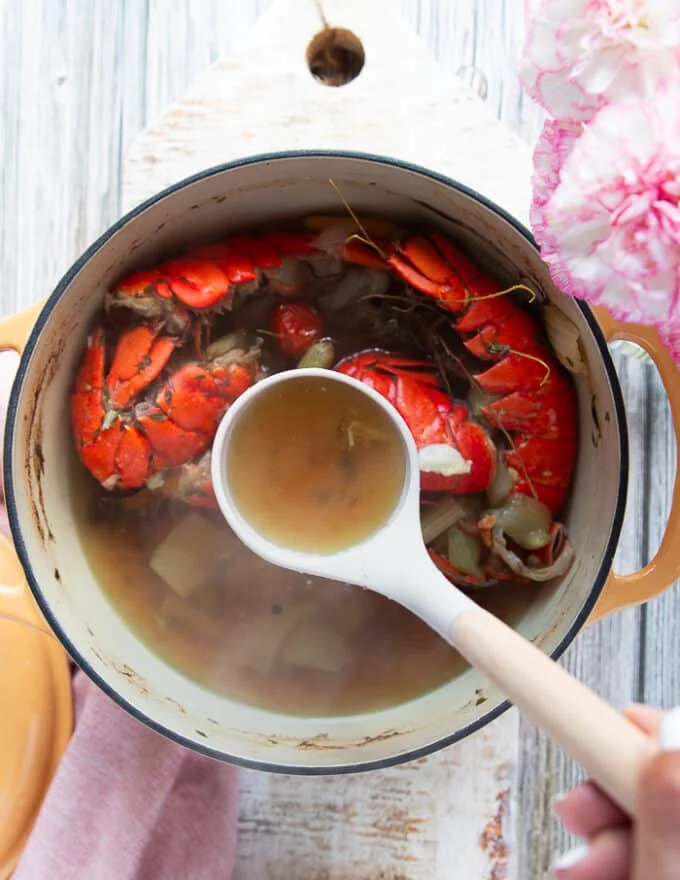 A ladle placed in the post of lobster stock showing how golden and rich the color of the stock is so it's ready