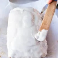 A hand spreading the glaze evenly over the pumpkin bread using a spatula