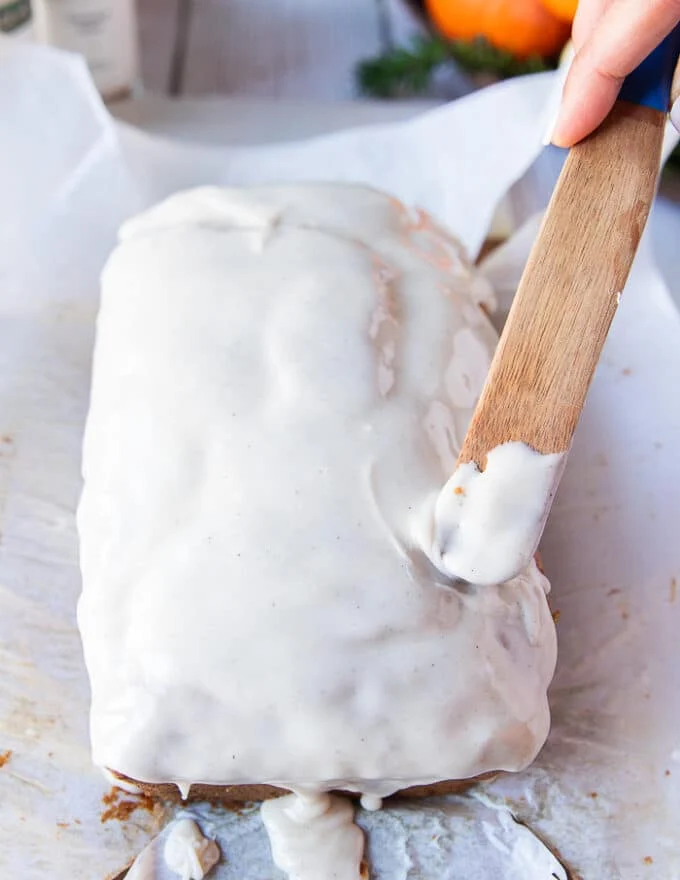 A hand spreading the glaze evenly over the pumpkin bread using a spatula