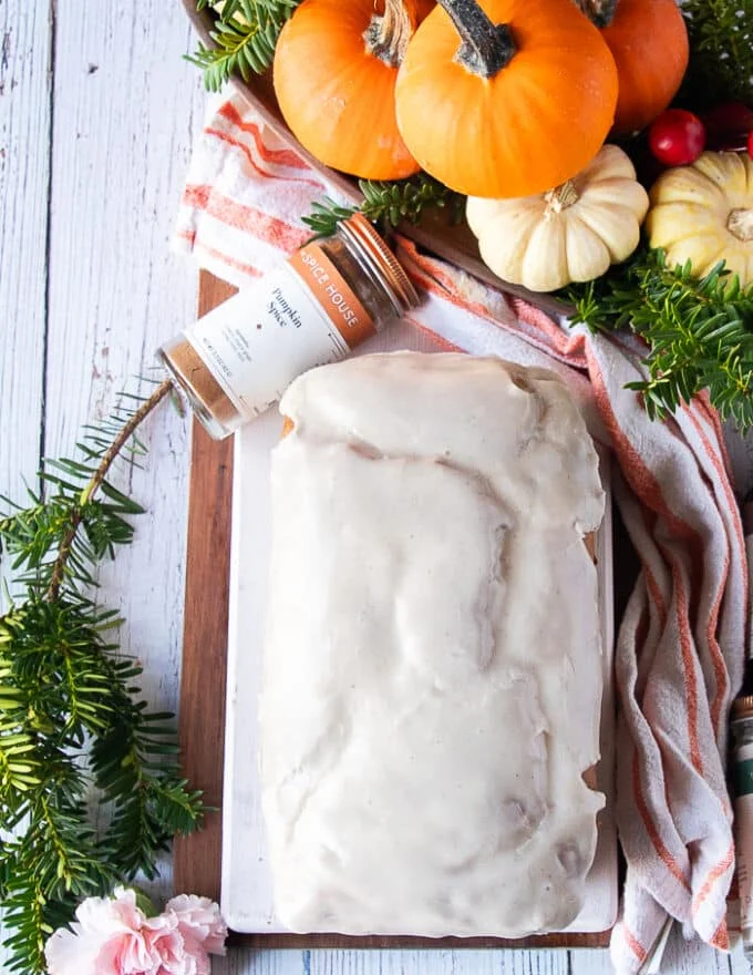 ready and glazed whole pumpkin bread on a wooden board surrounded by small pumpkins and some fall leaves