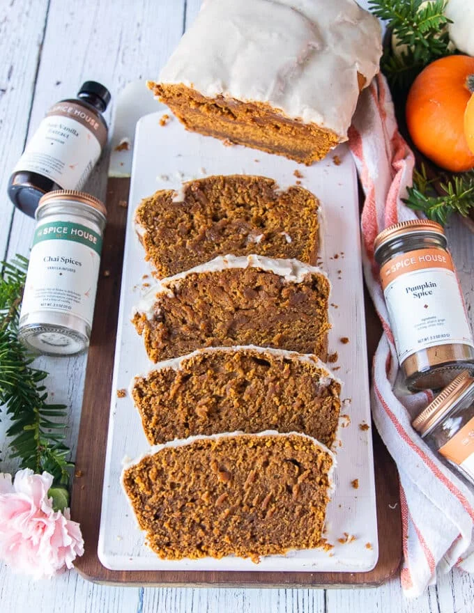 top view of the pumpkin bread, half of it sliced into half inch thick slices and arranged overlapping, while the other half in tact, surrounded by mini pumpkins
