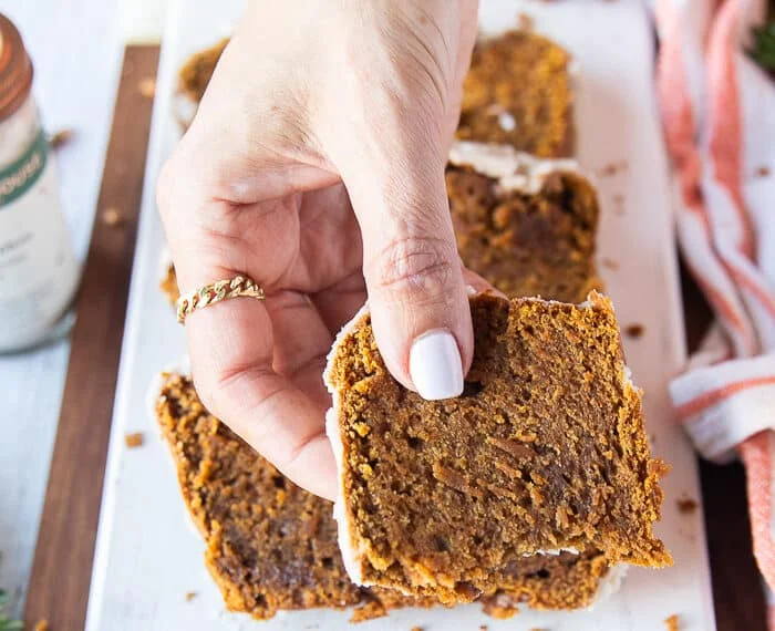 A hand holding a bitten piece of pumpkin bread recipe close up showing up the texture