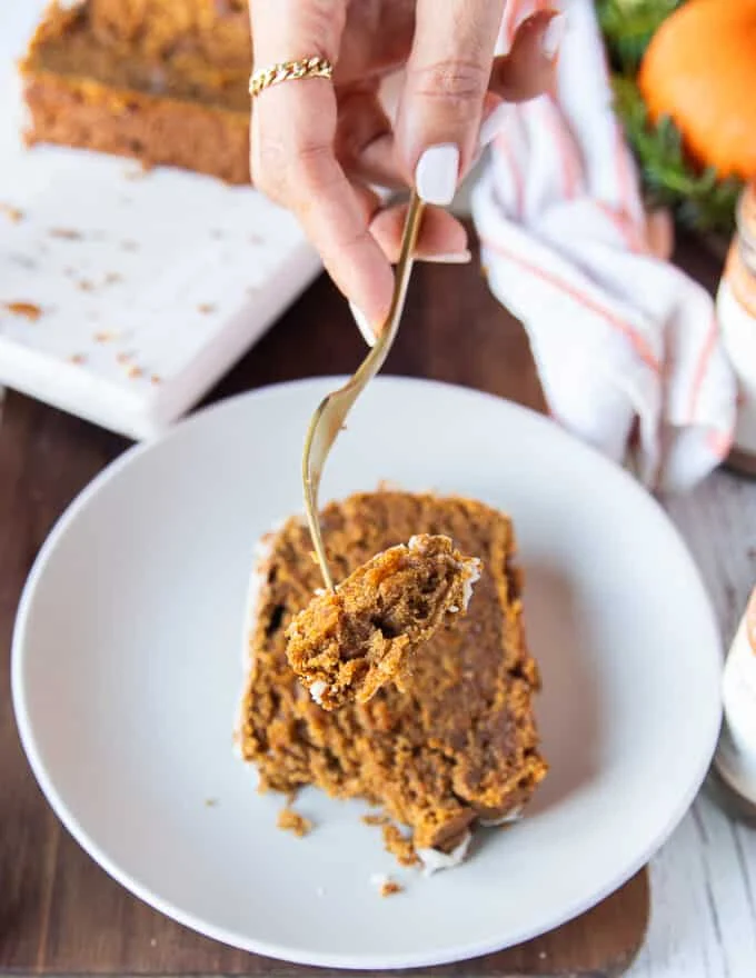 A hand holding a fork with a chunk of pumpkin bread showing close up the texture and how soft and moist the bread is.