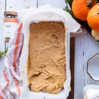 The pumpkin bread batter poured into a load pan lined with parchment paper and ready to bake