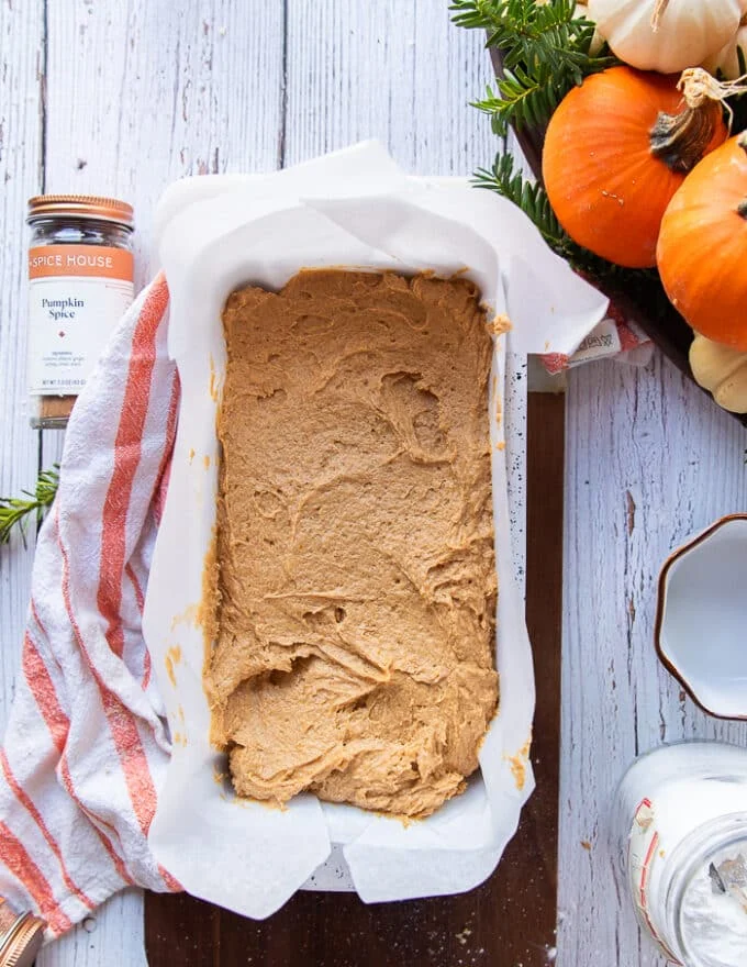 The pumpkin bread batter poured into a load pan lined with parchment paper and ready to bake