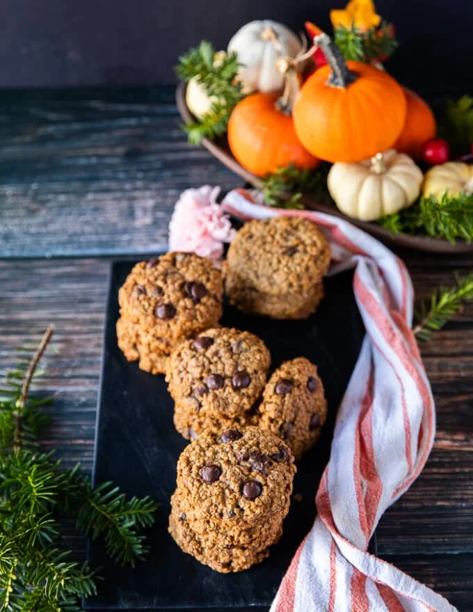 A plate of pumpkin oatmeal cookies surrounded by baby pumpkins and fall leaves