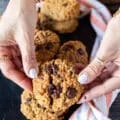 A hand holding a pumpkin Oatmeal cookie close up and breaking it apart to show the melted chocolate chunks and how soft the cookie are