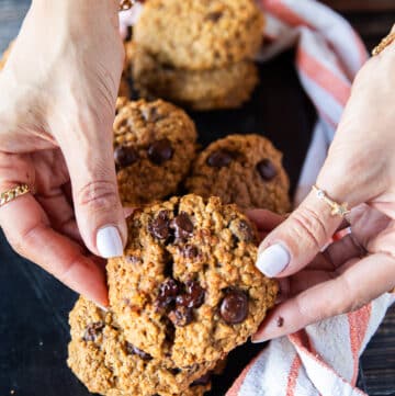 A hand holding a pumpkin Oatmeal cookie close up and breaking it apart to show the melted chocolate chunks and how soft the cookie are