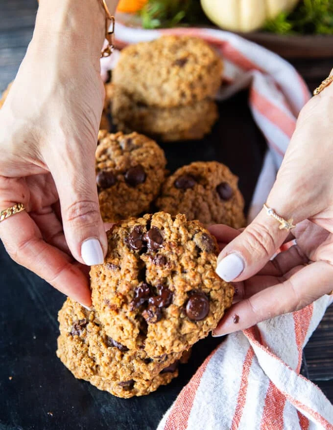 A hand holding a pumpkin Oatmeal cookie close up and breaking it apart to show the melted chocolate chunks and how soft the cookie are