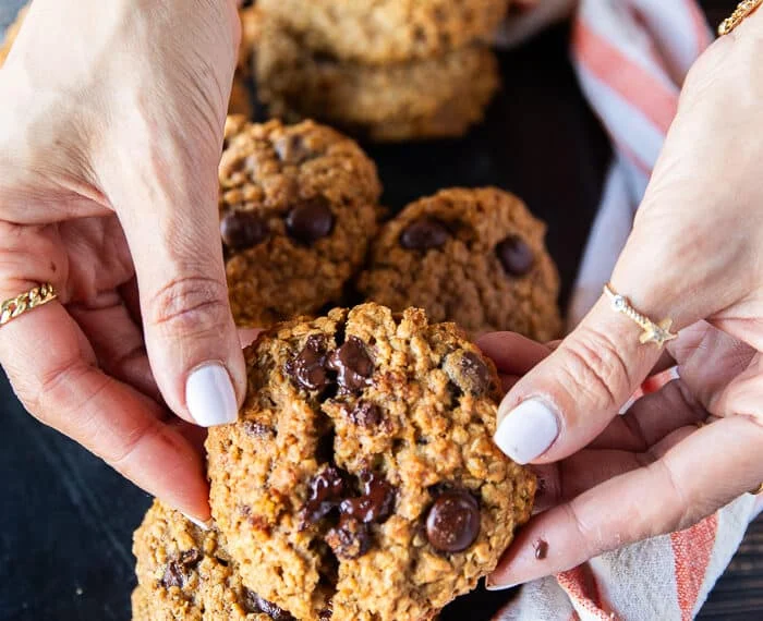 A hand holding a pumpkin Oatmeal cookie close up and breaking it apart to show the melted chocolate chunks and how soft the cookie are