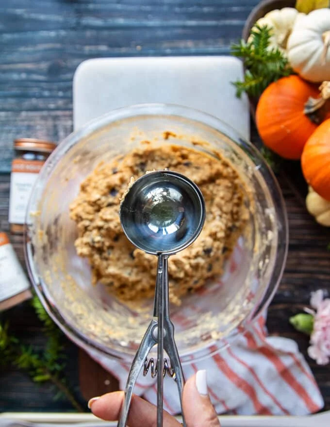 A hand holding a one inch ice cream scoop to scoop up the batter