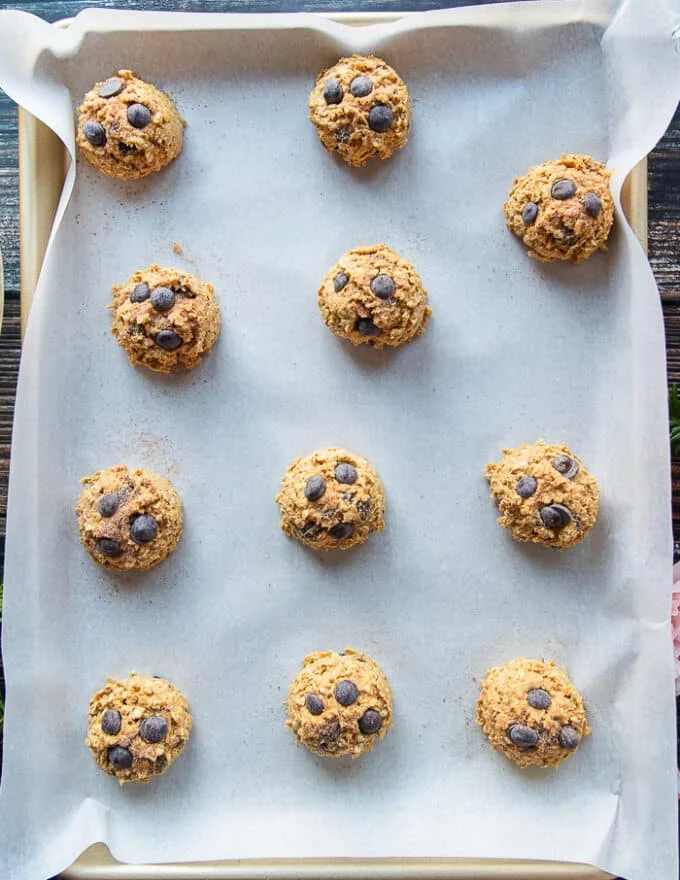 Scooped pumpkin oatmeal chocolate chip cookies on a baking sheet ready to bake