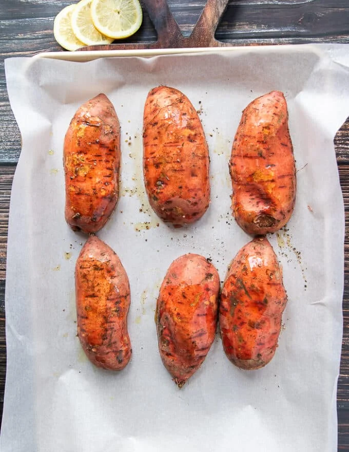 seasoned cut sweet potatoes placed on a parchment lined baking sheet, cut side down