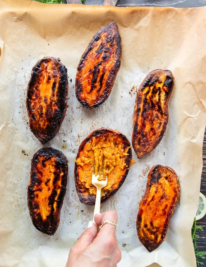 A hand holding a fork and smashing the inside of the sweet potatoes to prepare them for stuffing