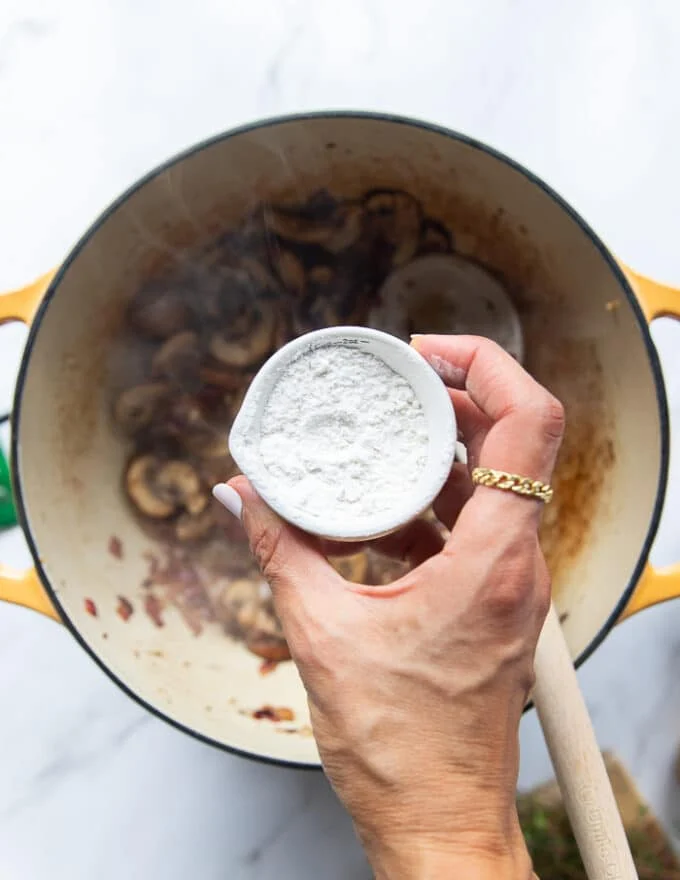 A hand sprinkling flour over the onion and mushrooms