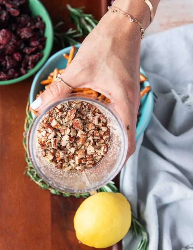 A hand holding a mini processor bowl showing the pecans processed into bite size