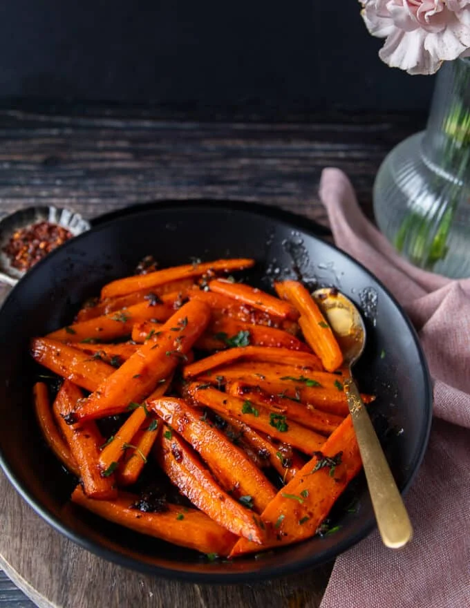 side view of a plate of honey roasted carrots with a serving spoon