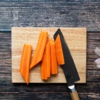 carrots being cut on a cutting board with a sharp knife