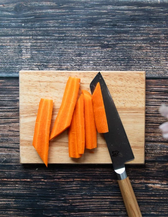 carrots being cut on a cutting board with a sharp knife