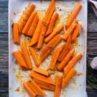 The carrots are spread on a baking sheet and half of the glazed is poured on top of that
