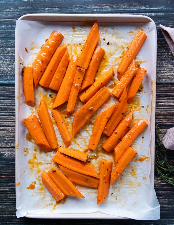 The carrots are spread on a baking sheet and half of the glazed is poured on top of that